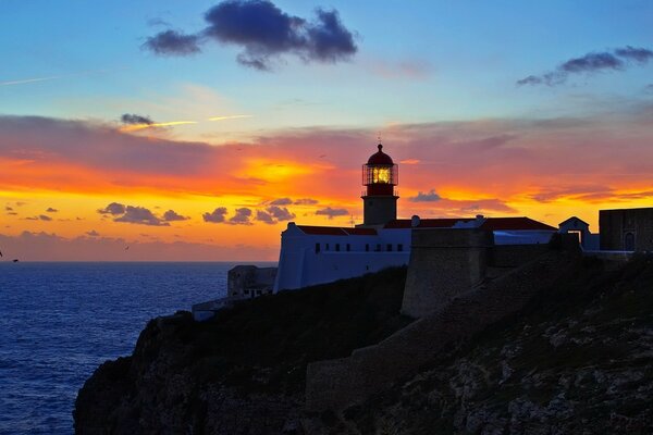 Faro en la orilla del mar en medio de la puesta de sol y las nubes