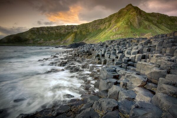 Green mountains on the stone shore of stormy water