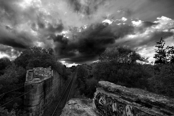 Image en noir et blanc avec un chemin de fer graffiti et des nuages d orage