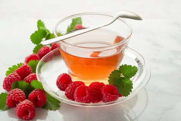 Tasse Tee und Himbeerbeeren auf Untertasse und Tisch