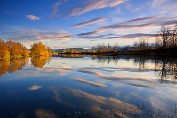 Nuvole e alberi si riflettono nel lago