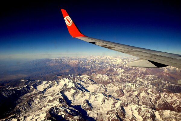 The wing of an airplane in the sky over the mountains