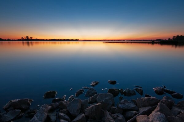 Lago en una hermosa puesta de sol. Piedras en la orilla del lago