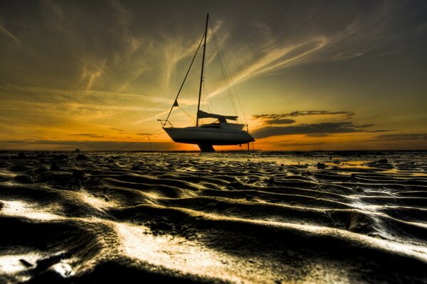 A boat with a lowered sail on a yellow sky background