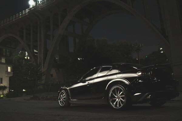 Black Mazda at night under the bridge span