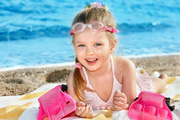 Chica de ojos azules en la playa con gafas de natación yace en la playa y sonríe