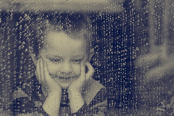 Niño mirando por la ventana lluviosa