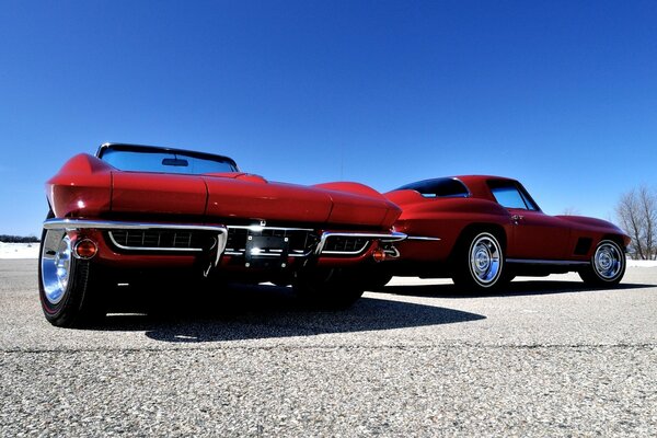 Two red Chevrolet Corvettes on a blue sky background