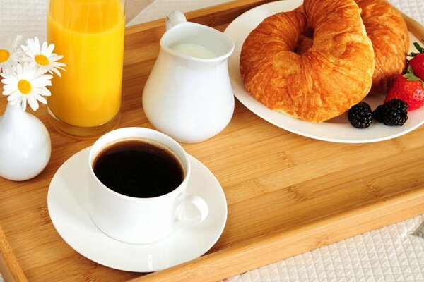 Tasse Kaffee mit Croissants, Beeren, Milch und Orangensaft zum Frühstück im Bett serviert