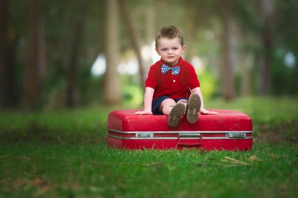 Garçon assis sur une valise rouge