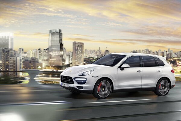 A light Porsche Cayenne rushes along the road against the background of the city