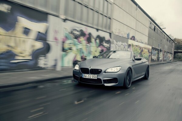 A convertible rushes along the road past graffiti