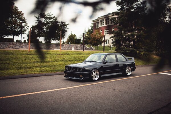 A black BMW car is driving near the house