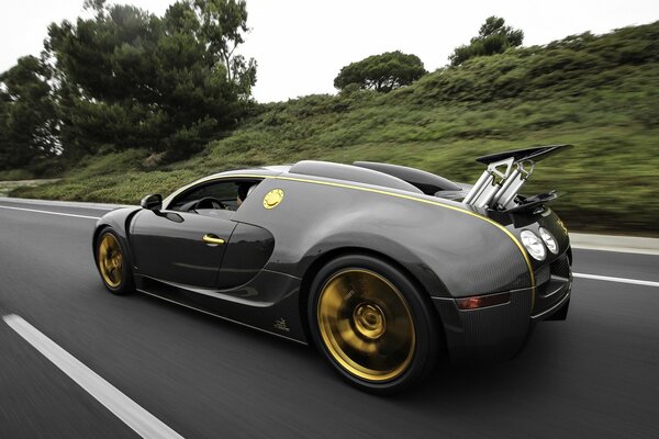 A black bugatti with golden wheels rushes along the road