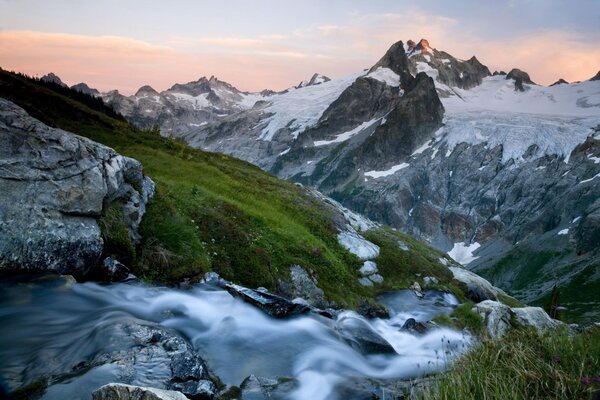 A stream in the middle of snow-capped mountains and grass