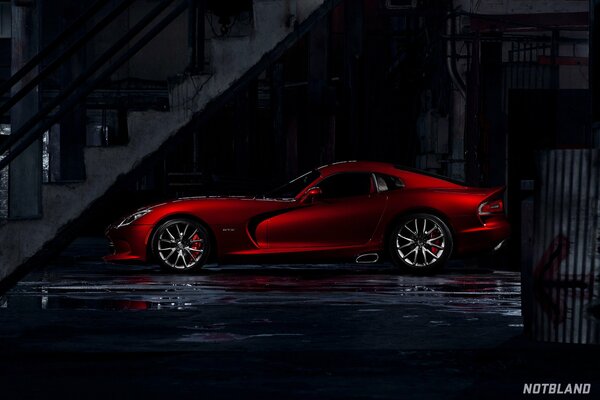 Voiture de sport rouge sous les escaliers dans la ville sombre après la pluie