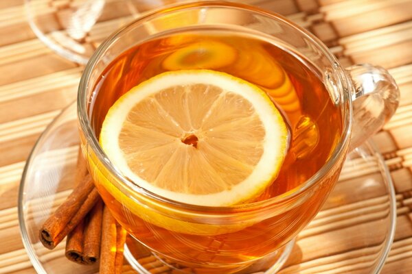 Té en una taza transparente con una rodaja de limón y palitos de canela