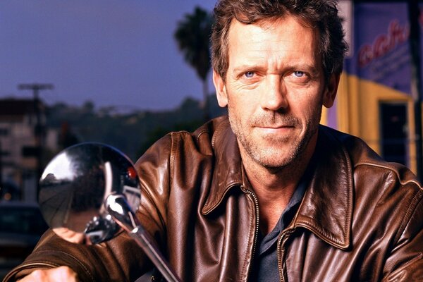 Hugh Laurie dans une veste en cuir sur une moto