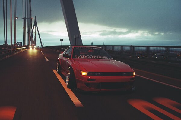 Ein roter Nissan fährt bei Sonnenuntergang über eine Hängebrücke