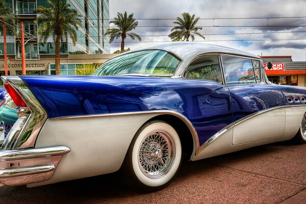 Buick azul y blanco se encuentra en la calle con palmeras