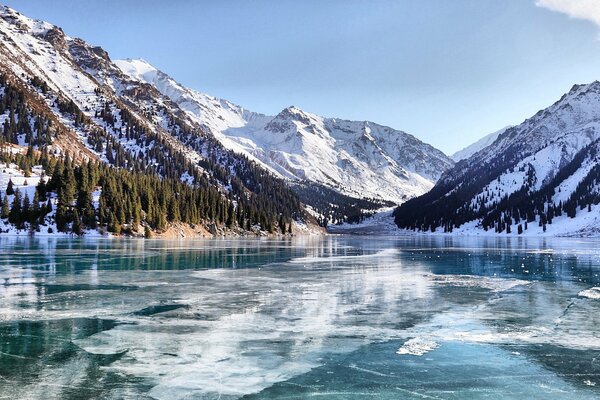 Ein zugefrorener See, die Berge sind mit Schnee bedeckt, an den Hängen der Berge ein Wald. sonniger Tag