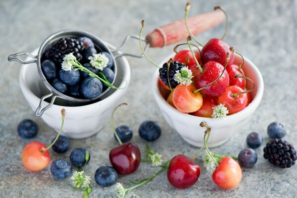 Bayas: arándanos, moras y cerezas en tazones de vidrio blanco