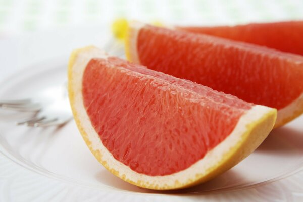 Gajos de pomelo en un plato sobre un fondo blanco