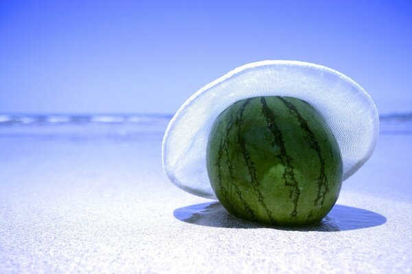 Sandía solitaria en una playa de arena con un sombrero normal