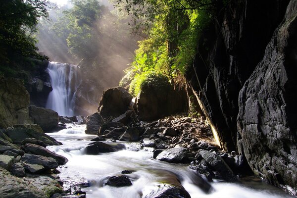 Los rayos del sol iluminan una cascada entre las rocas