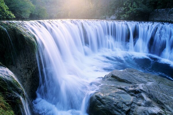 The wide waterfall is surrounded by stone cliffs