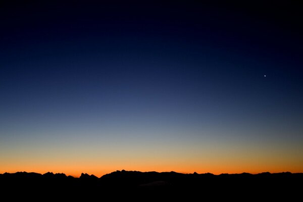 Ein schwarzer Horizontstreifen vor dem Hintergrund der orangefarbenen Linie der aufgehenden Sonne und des blauen Himmels, der in die Nacht übergeht