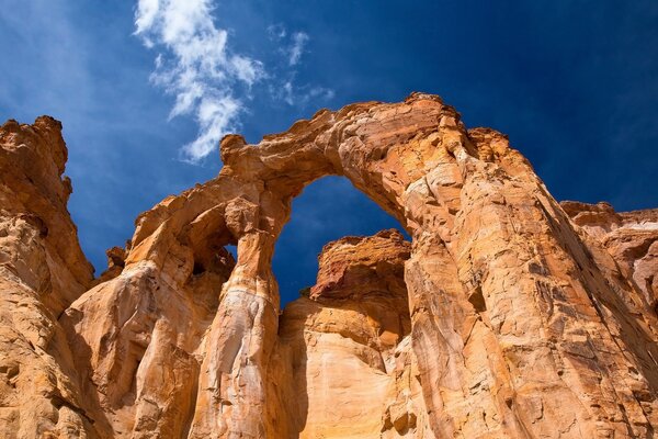 An arch in an orange rock against a blue sky with light white clouds