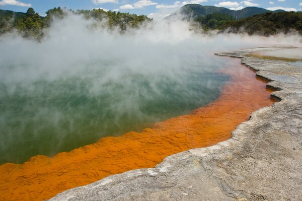 Ein See mit einem orangefarbenen Boden, aus dem ein Geysir schlägt