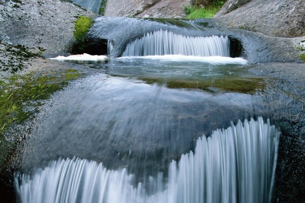 A mountain stream flows down over moss-covered rocks