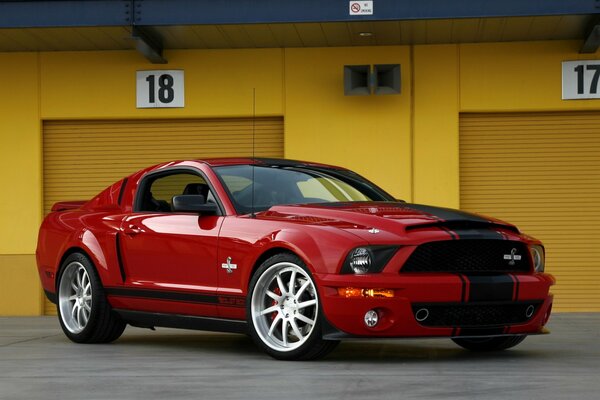 Ford Mustang rouge à côté debout sur fond de garages jaunes