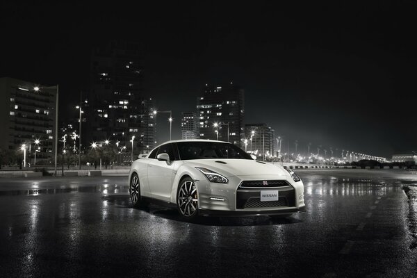Nissan GT-r blanc sur asphalte mouillé sur fond de ville de nuit