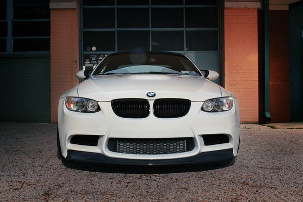 Devant une BMW M3 blanche sur fond de porte en brique