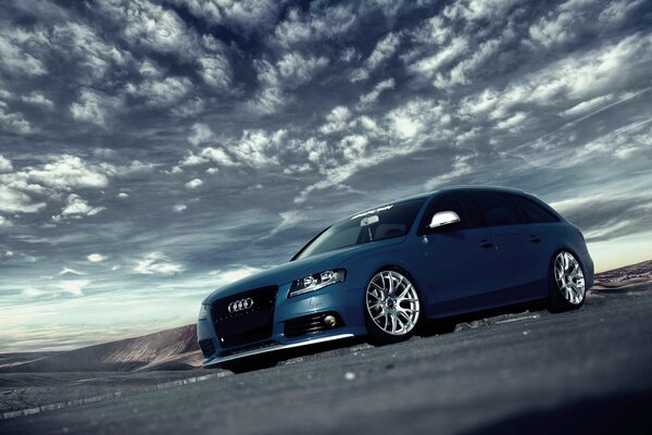 Blue audi on the background of the sky with feather clouds