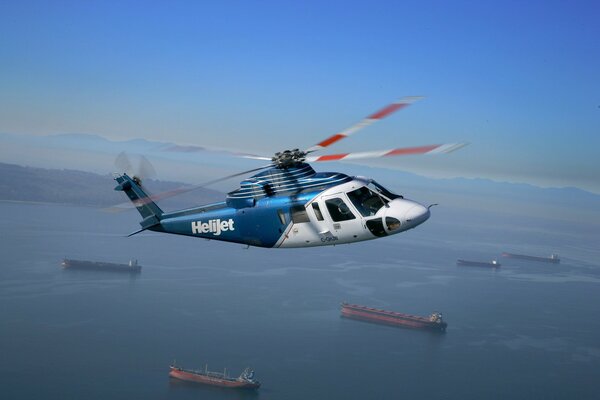 Blue S-76 helicopter in flight over the ocean