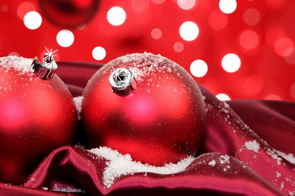 Rote Christbaumkugeln im Schnee auf rotem Stoff