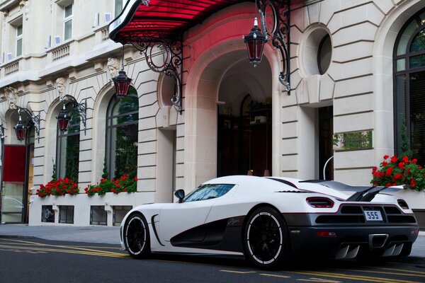 White koenigsegg stands at the white house with red flowers