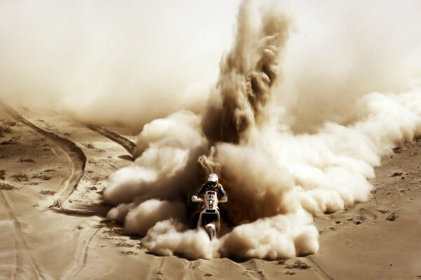 A motorcyclist rides through the desert scattering sand in different directions with a huge column of smoke