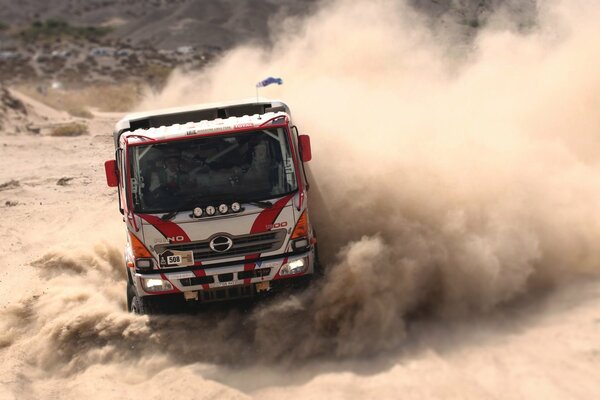 A sports truck is dusting on the highway on the sand