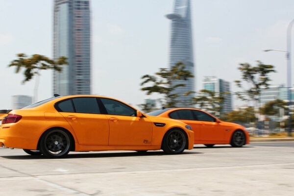 Two orange cars are racing along the road at high speed