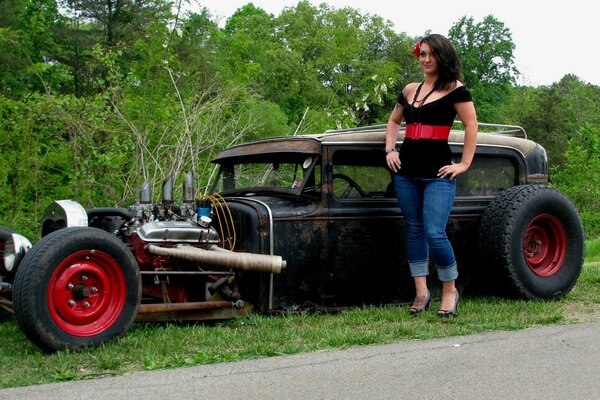 A beautiful girl in jeans is standing near a car in nature