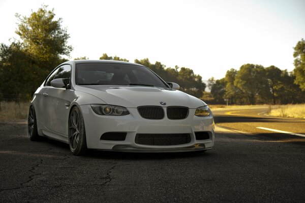 A white BMW is parked on an asphalt road