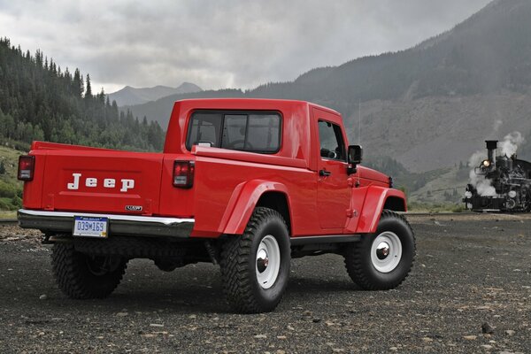 Jeep J-12 pick-up in rosso vista posteriore sullo sfondo delle montagne