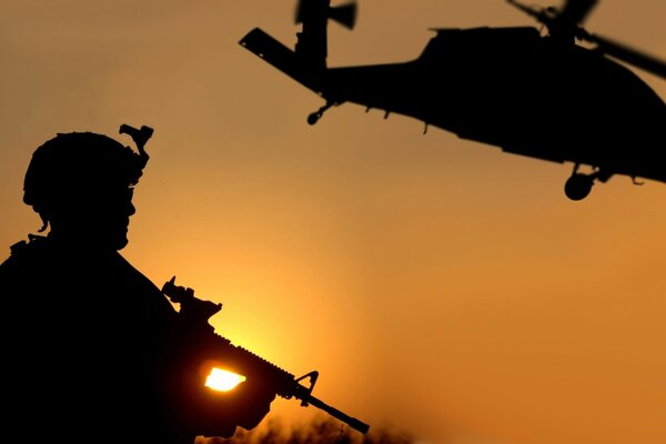 A beautiful sunset, a soldier is standing and a helicopter is flying