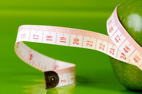 A green apple in a measuring tape on a green background