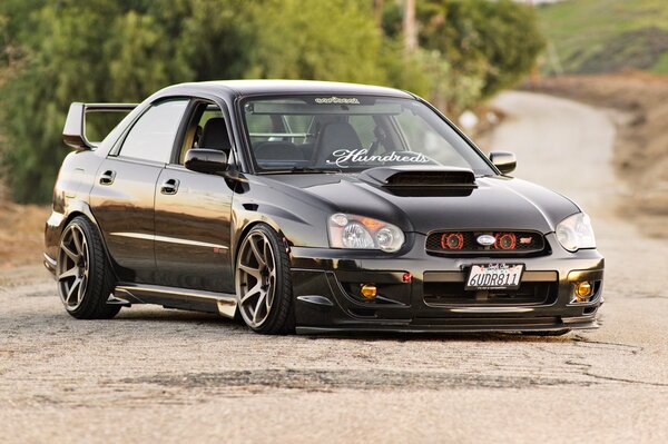 A black subaru impreza is standing on the road